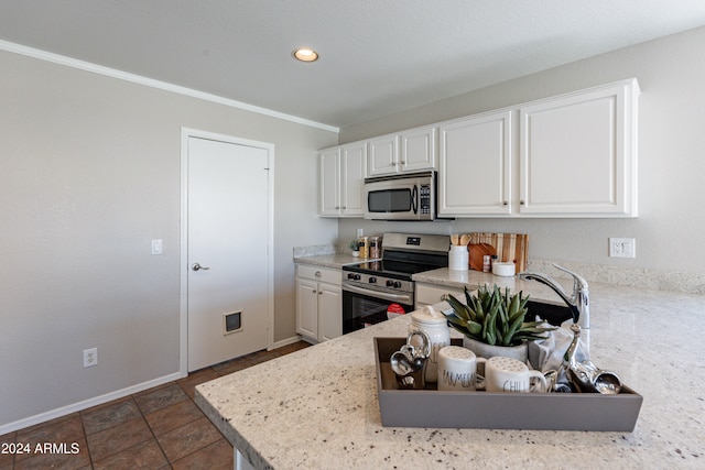 kitchen with dark tile patterned flooring, white cabinetry, stainless steel appliances, light stone counters, and ornamental molding