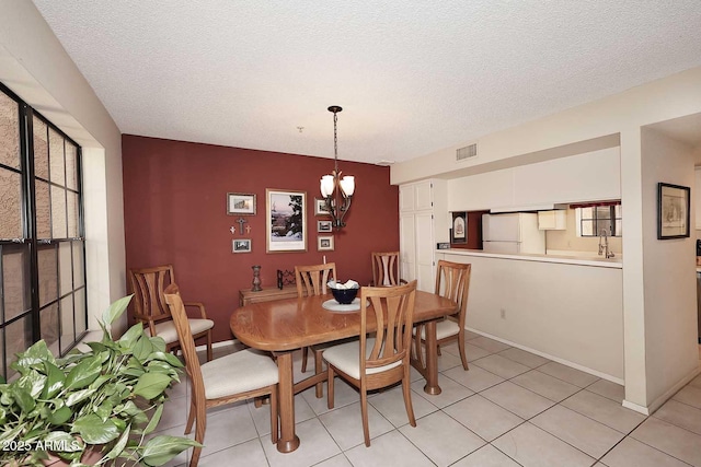 dining room with a textured ceiling, visible vents, light tile patterned floors, baseboards, and a notable chandelier
