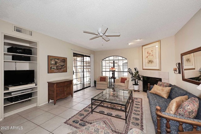 living area featuring ceiling fan, a textured ceiling, visible vents, built in features, and light tile patterned floors