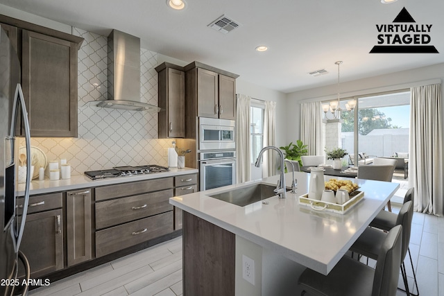 kitchen featuring stainless steel appliances, visible vents, a sink, and wall chimney exhaust hood