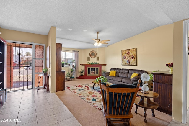 tiled living room with a textured ceiling, vaulted ceiling, ceiling fan, and a tiled fireplace