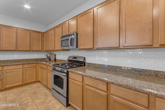 kitchen with light brown cabinets, appliances with stainless steel finishes, tasteful backsplash, light tile patterned flooring, and light stone counters