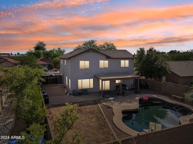 back of house at dusk with a patio area, a fenced backyard, a fenced in pool, and stucco siding