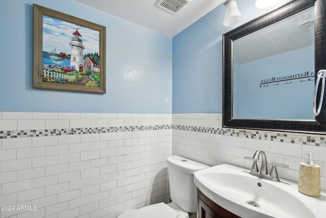 bathroom featuring visible vents, toilet, a wainscoted wall, vanity, and tile walls