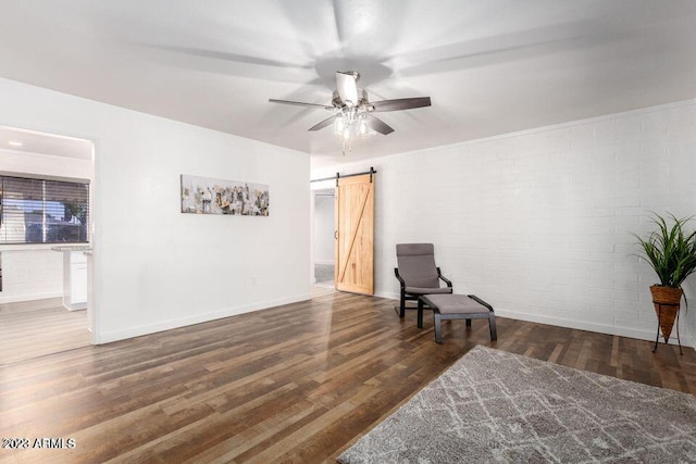 living area featuring a barn door, dark hardwood / wood-style flooring, ceiling fan, and brick wall