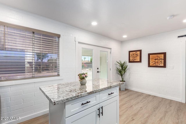 kitchen with light wood-type flooring, light stone countertops, a center island, and brick wall