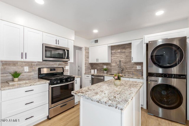 kitchen featuring white cabinets, stainless steel appliances, light wood-type flooring, and stacked washing maching and dryer