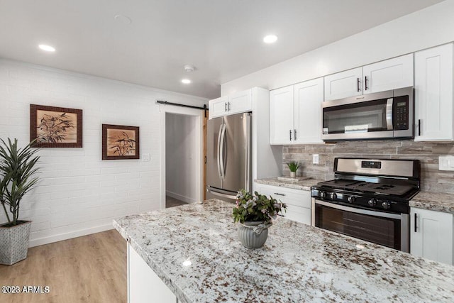 kitchen featuring appliances with stainless steel finishes, light hardwood / wood-style floors, white cabinetry, a barn door, and light stone countertops