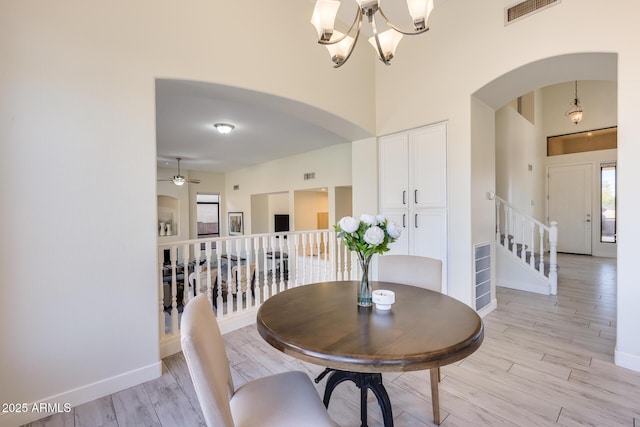 dining area featuring a high ceiling, ceiling fan with notable chandelier, and light hardwood / wood-style floors