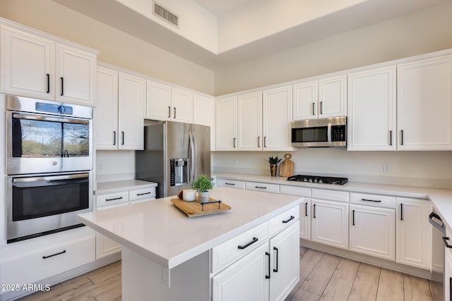 kitchen featuring white cabinetry, light wood-type flooring, stainless steel appliances, and a kitchen island