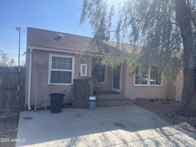 view of front of property with a shingled roof, a patio, fence, and stucco siding