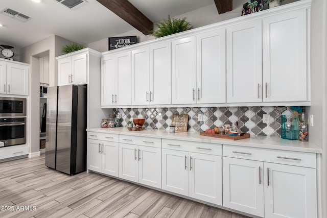 kitchen featuring tasteful backsplash, light countertops, visible vents, beamed ceiling, and stainless steel appliances