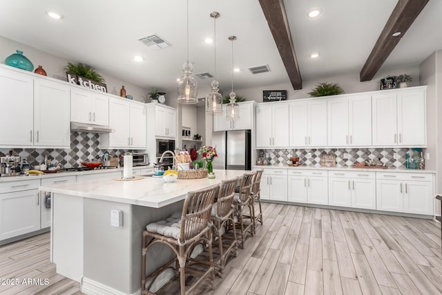kitchen featuring under cabinet range hood, freestanding refrigerator, backsplash, and visible vents