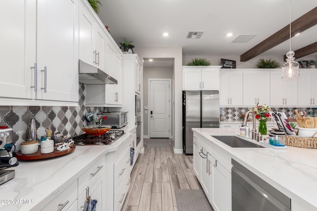 kitchen featuring white cabinets, under cabinet range hood, visible vents, appliances with stainless steel finishes, and a sink