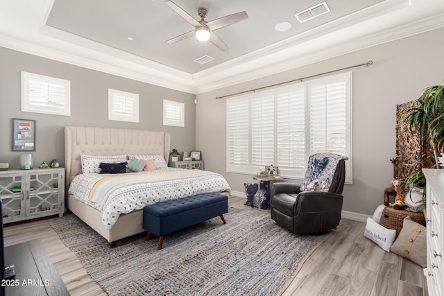 bedroom featuring ornamental molding, a tray ceiling, wood finished floors, and visible vents