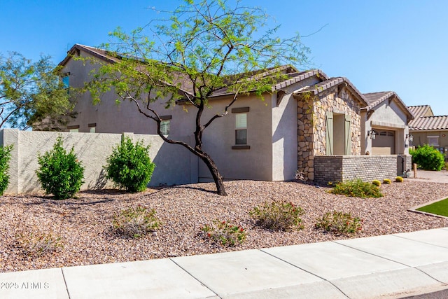 view of side of home featuring a tiled roof, an attached garage, stone siding, fence, and stucco siding