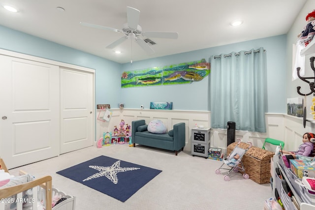 recreation room with a decorative wall, a ceiling fan, a wainscoted wall, and carpet floors