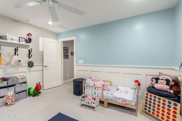 carpeted bedroom with visible vents, a wainscoted wall, and ceiling fan