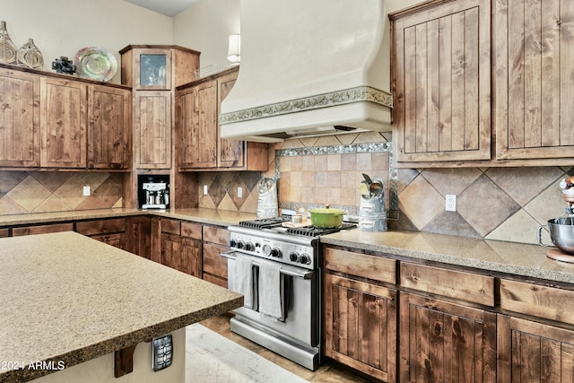 kitchen with custom exhaust hood, backsplash, and stainless steel stove