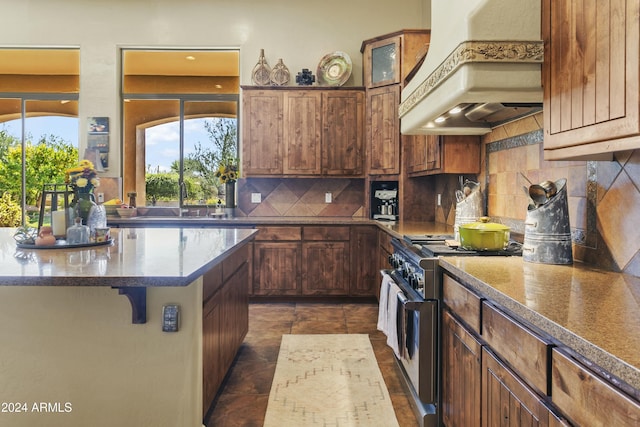 kitchen featuring premium range hood, sink, high end stainless steel range, decorative backsplash, and a kitchen bar