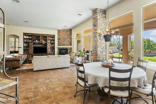 dining room featuring plenty of natural light, a stone fireplace, built in shelves, and an inviting chandelier