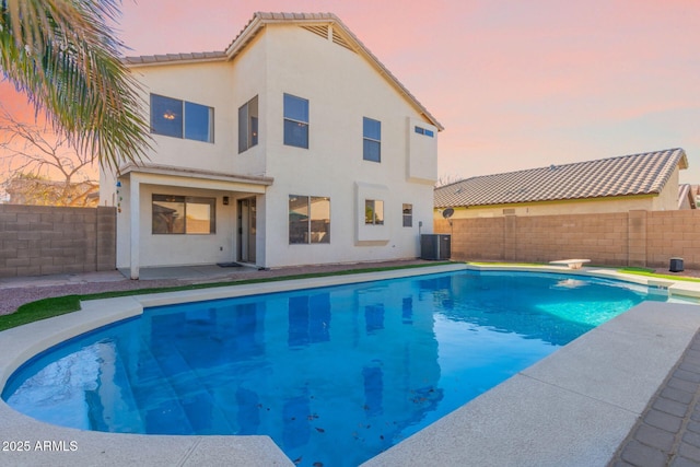 pool at dusk with cooling unit and a diving board