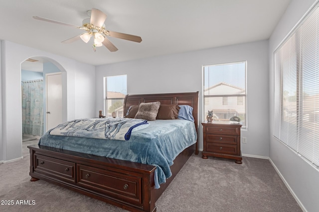 bedroom with multiple windows, connected bathroom, light colored carpet, and ceiling fan