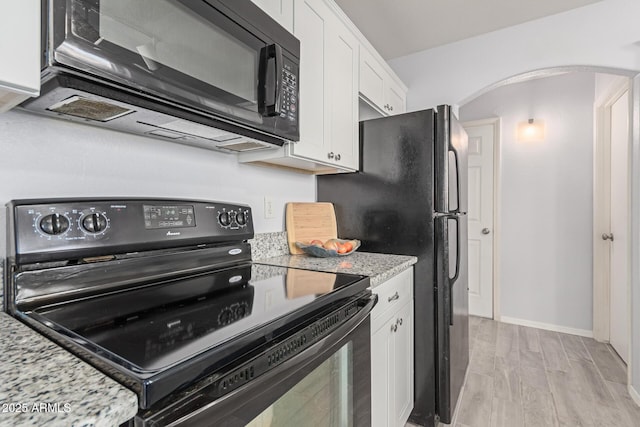 kitchen with white cabinetry, light stone counters, black appliances, and light hardwood / wood-style floors