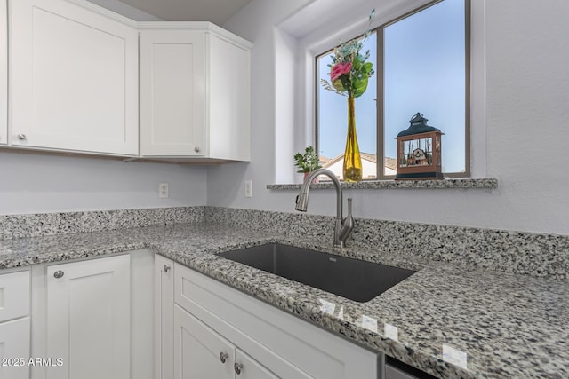 kitchen featuring light stone counters, sink, and white cabinets