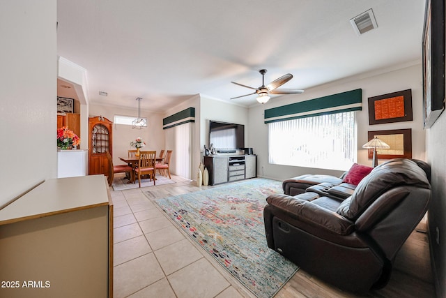 living room featuring light tile patterned floors, a ceiling fan, visible vents, and crown molding