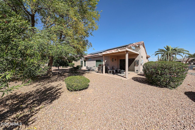 rear view of house featuring a patio area, a tile roof, roof mounted solar panels, and stucco siding