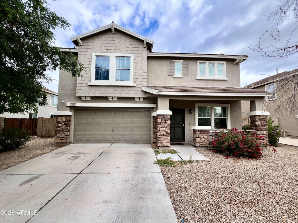 craftsman house featuring driveway, stone siding, stucco siding, and fence