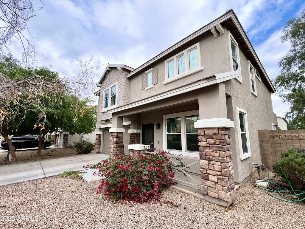 view of front facade featuring stone siding, stucco siding, driveway, and fence