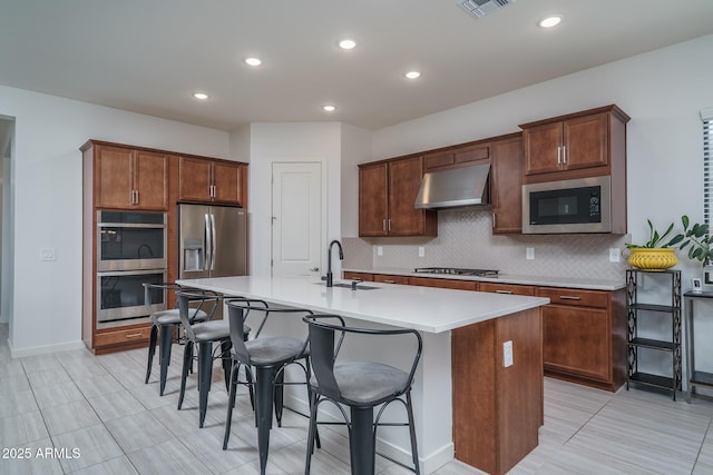 kitchen with tasteful backsplash, a sink, under cabinet range hood, appliances with stainless steel finishes, and a kitchen island with sink