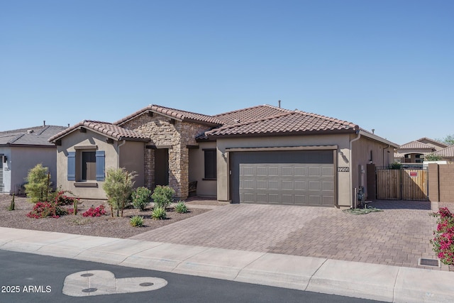 mediterranean / spanish house featuring stucco siding, a tile roof, decorative driveway, stone siding, and an attached garage