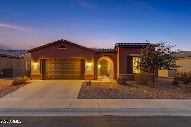 mediterranean / spanish house with concrete driveway, a tiled roof, an attached garage, and stucco siding