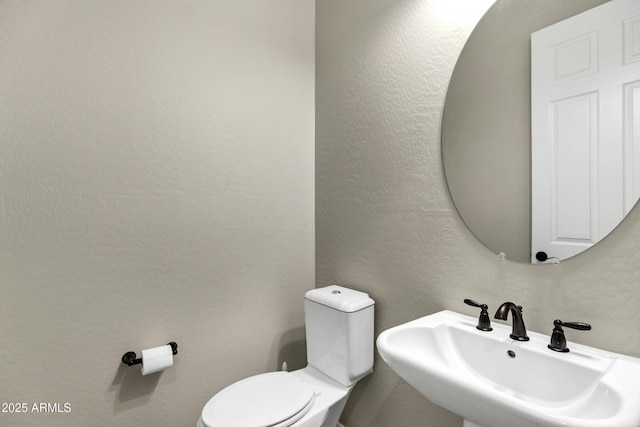 bathroom featuring a textured wall, a sink, and toilet