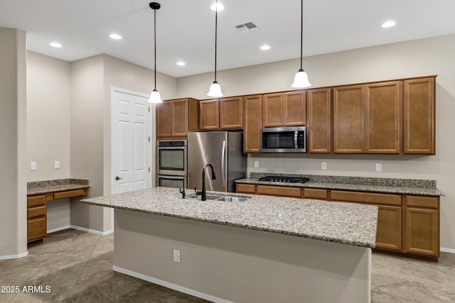 kitchen with pendant lighting, built in desk, a kitchen island with sink, and appliances with stainless steel finishes