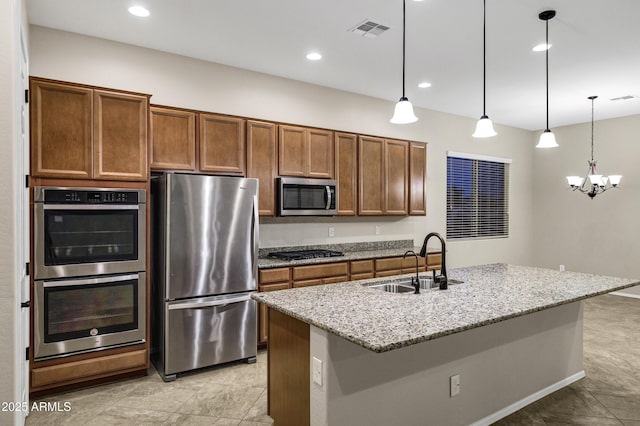 kitchen featuring sink, stainless steel appliances, light stone countertops, an island with sink, and decorative light fixtures