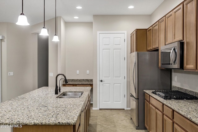 kitchen featuring decorative light fixtures, an island with sink, sink, light stone counters, and gas stovetop