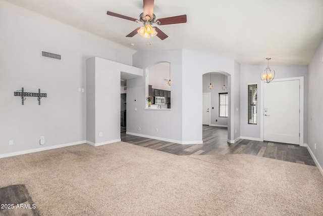 unfurnished living room featuring visible vents, arched walkways, baseboards, ceiling fan with notable chandelier, and dark carpet