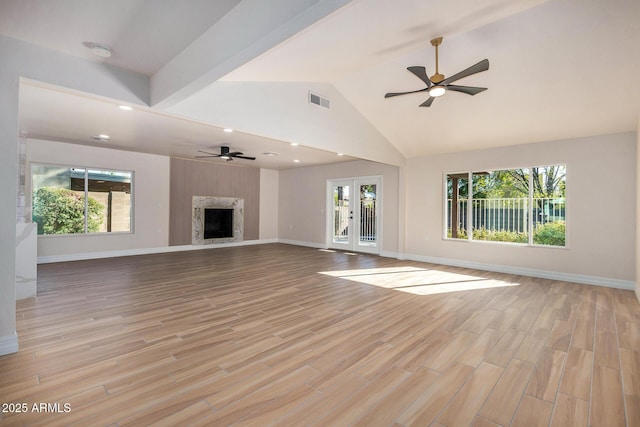 unfurnished living room with french doors, light wood-type flooring, ceiling fan, a high end fireplace, and lofted ceiling with beams