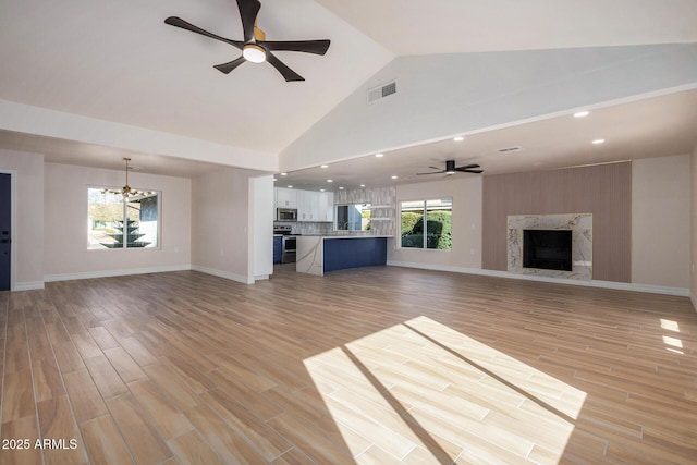 unfurnished living room featuring ceiling fan with notable chandelier, light hardwood / wood-style flooring, high vaulted ceiling, and a fireplace