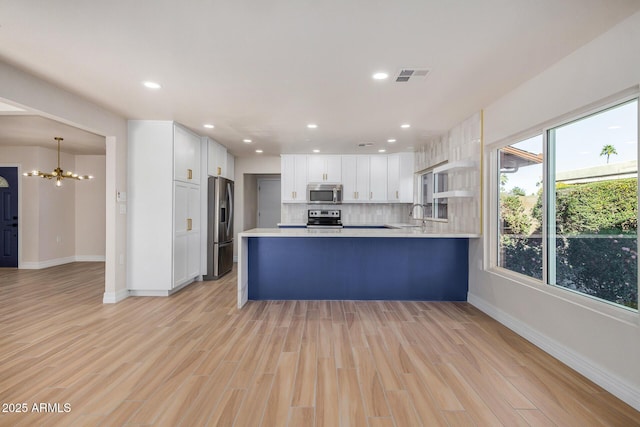 kitchen with decorative light fixtures, white cabinetry, kitchen peninsula, a notable chandelier, and appliances with stainless steel finishes