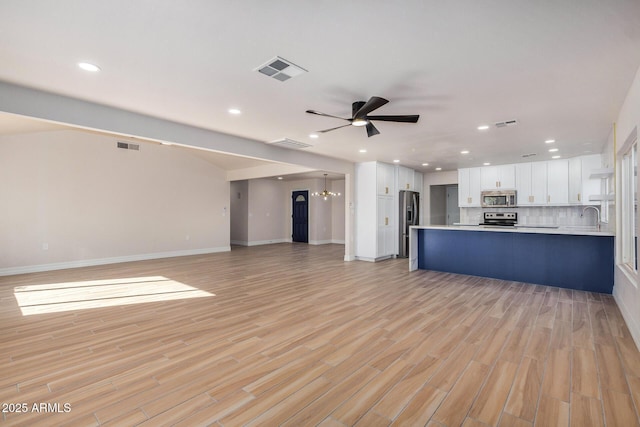 unfurnished living room with ceiling fan with notable chandelier and light hardwood / wood-style floors