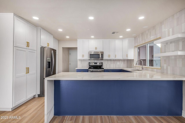 kitchen with stainless steel appliances, kitchen peninsula, sink, light hardwood / wood-style flooring, and white cabinetry