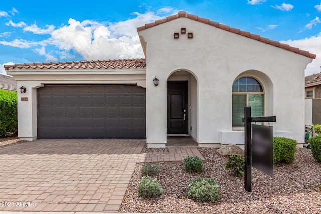 mediterranean / spanish-style house featuring stucco siding, driveway, a tile roof, and a garage