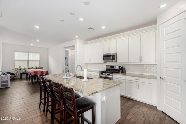 kitchen with visible vents, dark wood finished floors, decorative backsplash, appliances with stainless steel finishes, and a sink