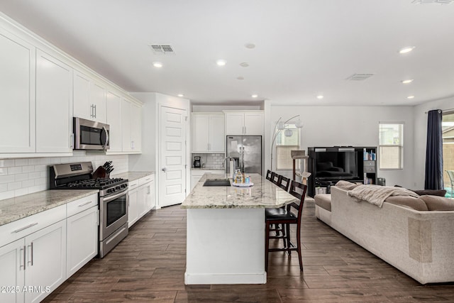 kitchen featuring visible vents, a sink, open floor plan, white cabinetry, and appliances with stainless steel finishes