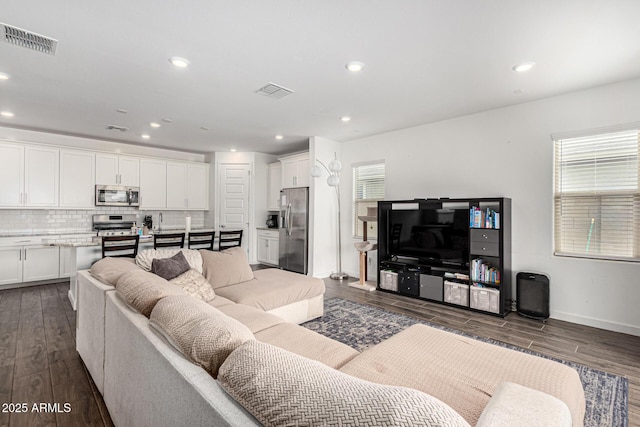 living area featuring visible vents, a healthy amount of sunlight, and dark wood-style flooring